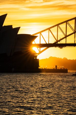 Sun bursting between the Opera House and Harbour Bridge at golden hour
