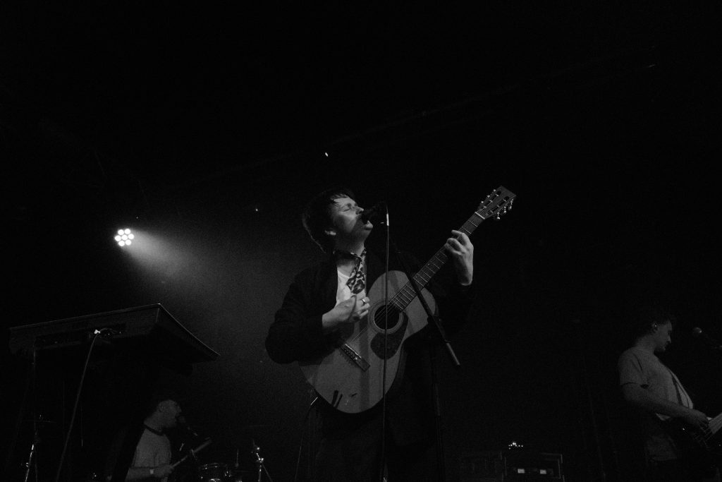 Performer playing acoustic guitar on stage under a spotlight at a live event